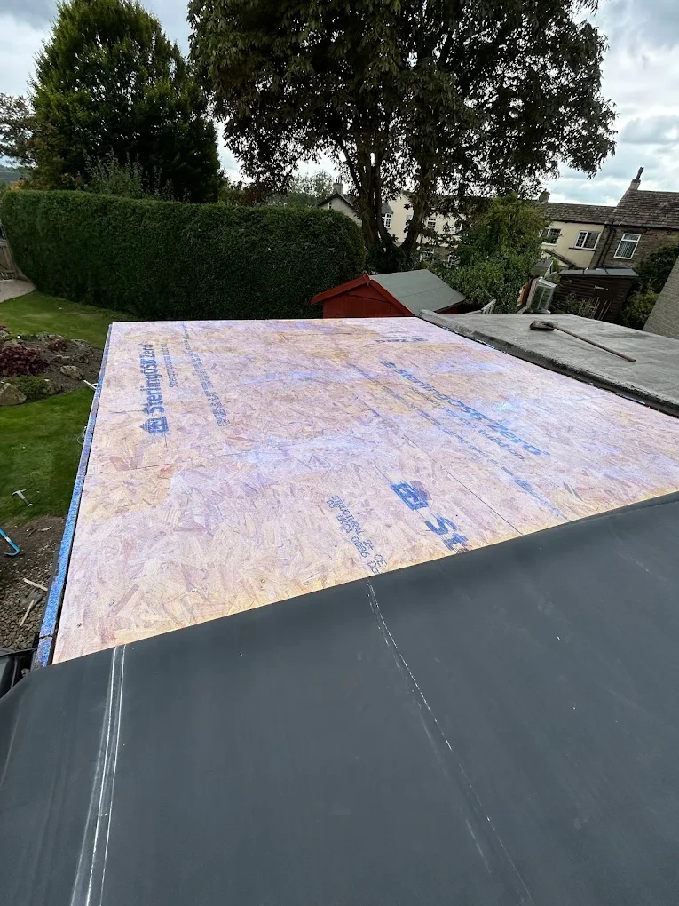 Flat roof installation in progress over a new OSB roof deck