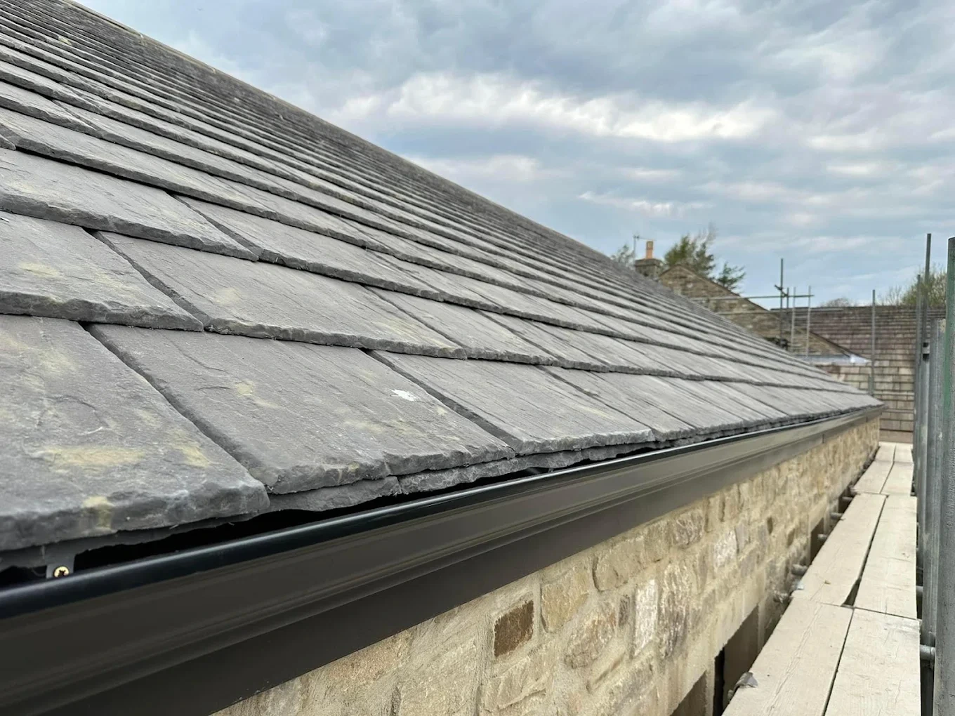 Replacement black guttering beneath a slate roof on a stone house