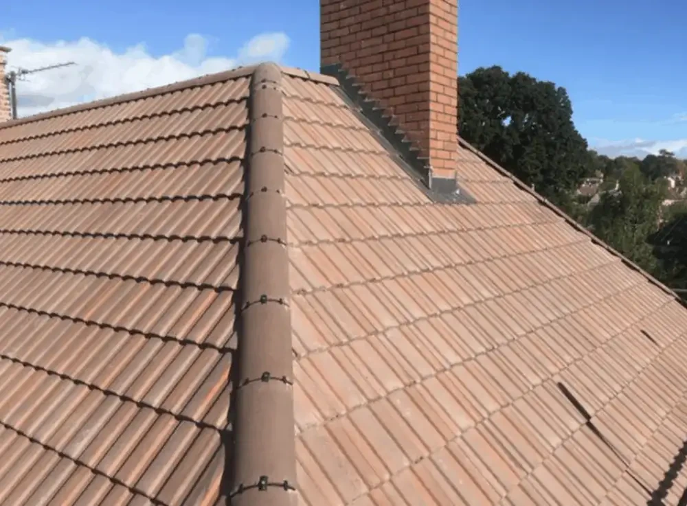 New terracotta tiled roof with ridge tiles beside a brick chimney