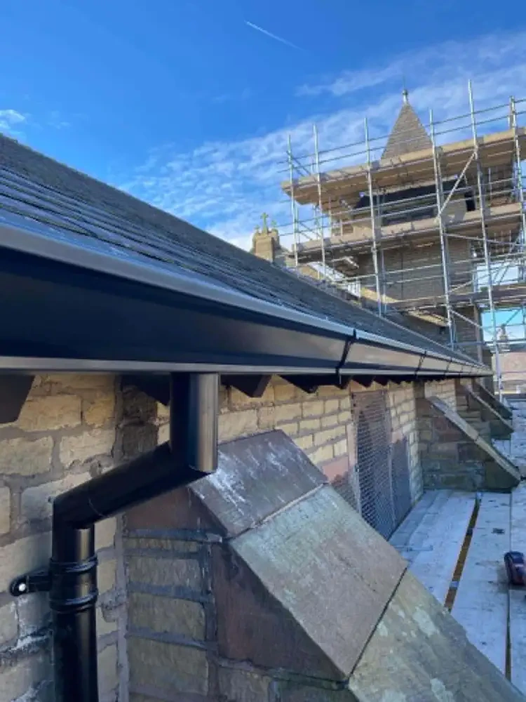 Black guttering and downpipe fitted to a stone building during scaffold works