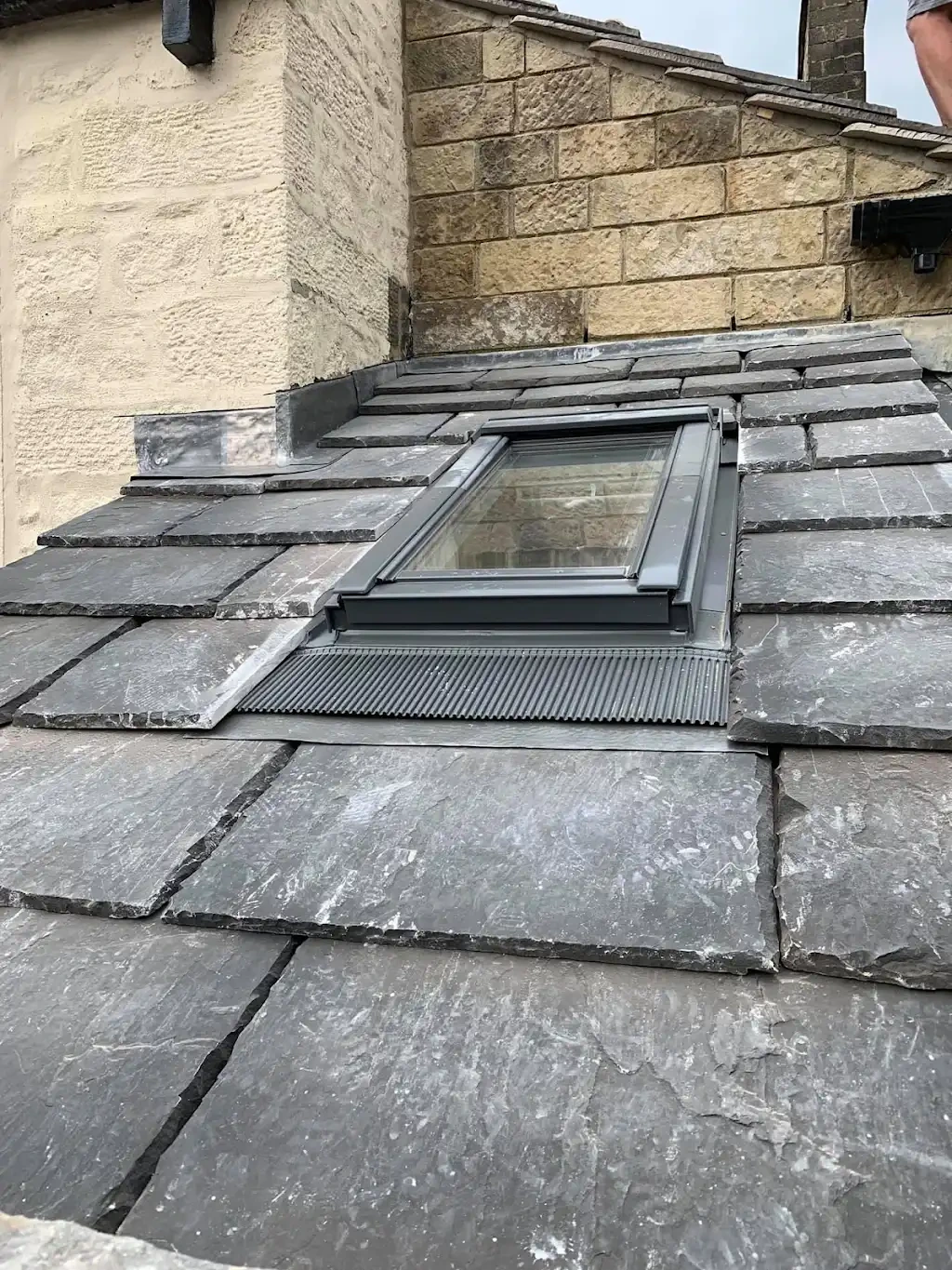 New lead flashing around a roof window on a slate roof by a stone chimney